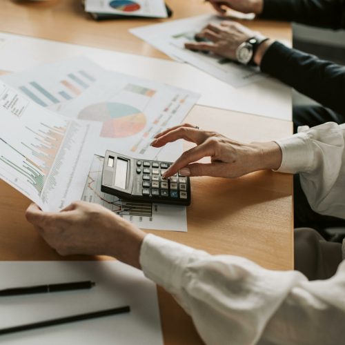 Hands performing financial calculations with charts and a calculator at a meeting table.